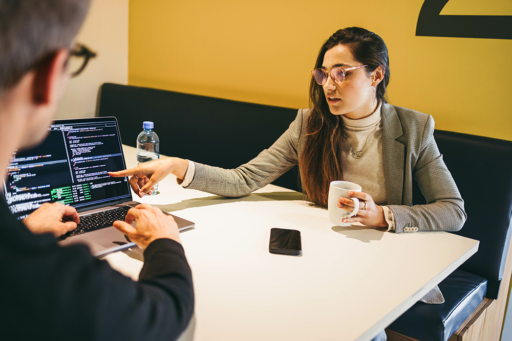 Woman showing laptop screen at meeting room table with another person